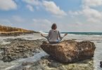 Lady yoga pose on boulder by ocean
